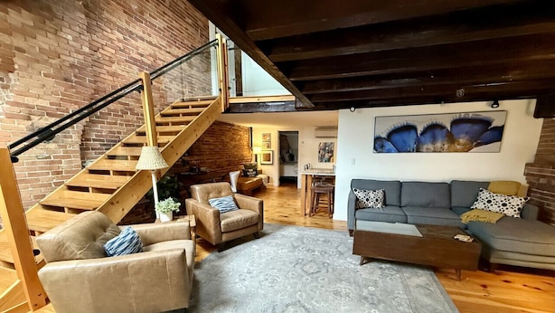 A loft-style living area with a staircase, leather sofas, a patterned rug, and a painting on the wall. - Superb Location! Heart of Old Port-Spacious Apartment (Portland)