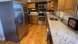 A modern kitchen with stainless steel appliances, wooden cabinets, granite countertops, and a wooden floor. - Superb Location! Heart of Old Port-Spacious Apartment (Portland)