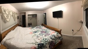 Un dormitorio con cama, una mesita de noche, una lámpara, televisor montado en la pared y un armario.