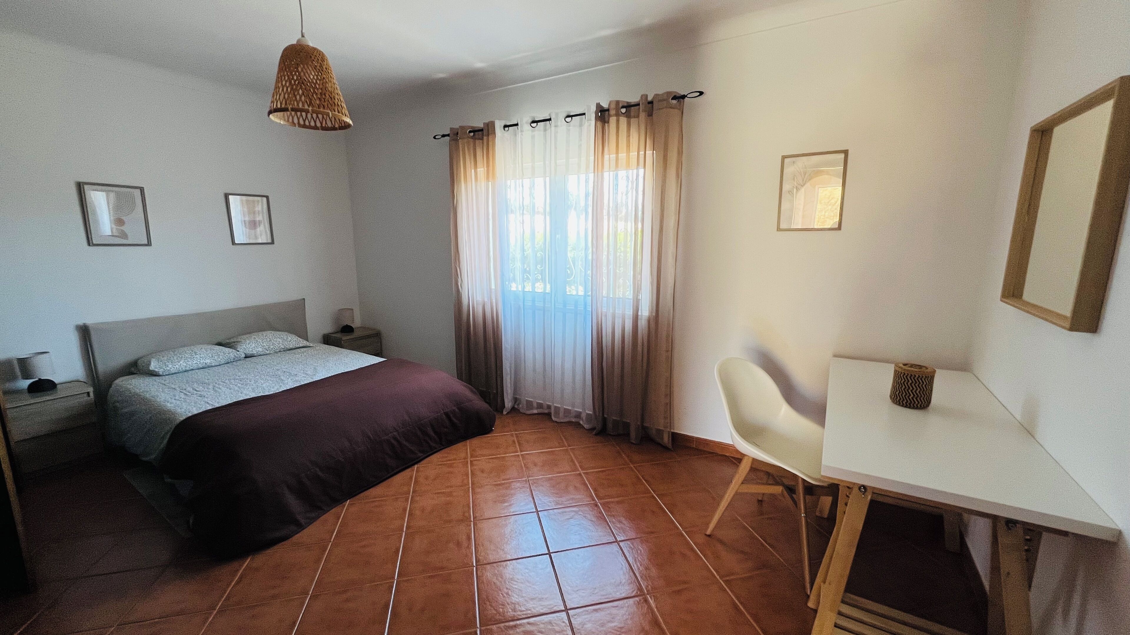 Un dormitorio con cama, mesita de noche, lámpara y escritorio con silla.