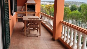 A balcony with a table and chairs, a grill, and a view of greenery and buildings. - Quinta dos Moledros (Figueira)