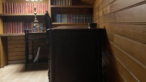 A room with wooden walls and a sloped ceiling, featuring a desk with a lamp, bookshelves, and a dark wooden cabinet. - Quiet country house animals welcome minimum nights 13! (Léotoing)