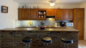 A kitchen with wooden cabinets, a tiled backsplash, a central island with stools, a microwave, and a chandelier. - Quiet country house animals welcome minimum nights 13! (Léotoing)
