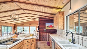 A kitchen with wooden cabinets, a large island, and a view of a red barn through a glass door. - Groveland Cabin w/ Outdoor Perks & Game Room (Groveland)
