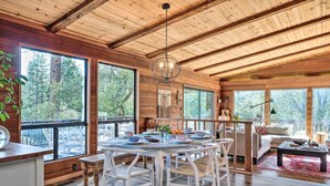 A spacious wooden cabin with large windows, a dining area with white chairs, and a cozy living space with a sofa and coffee table. - Groveland Cabin w/ Outdoor Perks & Game Room (Groveland)