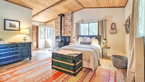 A cozy bedroom with a large bed, a dresser, a suitcase, and a fireplace. - Groveland Cabin w/ Outdoor Perks & Game Room (Groveland)