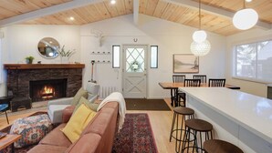 A spacious living room with a fireplace, a dining area with a high wooden ceiling, and a kitchen with a large island. - Pino Point Steps to Tahoe Beaches (Kings Beach)