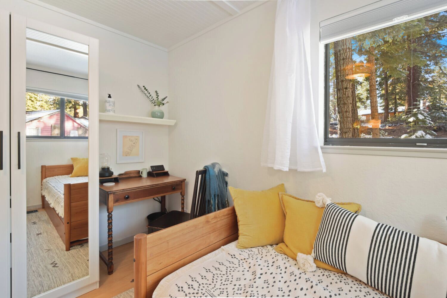Un dormitorio con cama, escritorio, silla y ventana con vista a árboles.