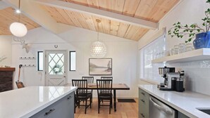 A modern kitchen with a central island, wooden ceiling, and a dining area with chairs and a table. - Pino Point Steps to Tahoe Beaches (Kings Beach)