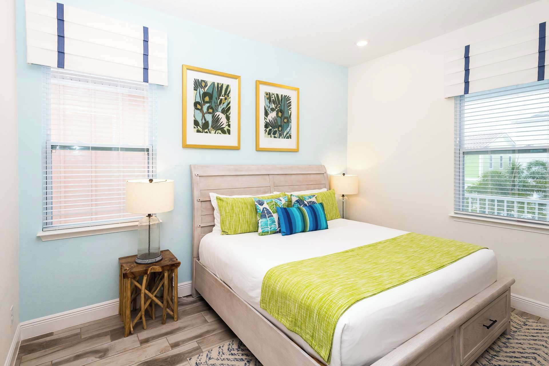 A bedroom with a bed, two bedside lamps, a small wooden table, and two framed pictures on the wall.