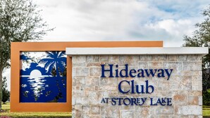 A sign for Hideaway Club at Storey Lake, featuring a stone wall and a decorative panel with a sunset scene. - Enchanted Clock Tower (Kissimmee)