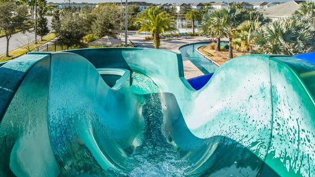 A water slide with a curved design, surrounded by palm trees and a residential area in the background. - Enchanted Clock Tower (Kissimmee)