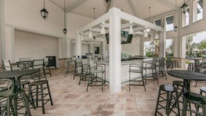 A spacious outdoor dining area with multiple tables and chairs, a central bar area, and a high ceiling with hanging lanterns. - Enchanted Clock Tower (Kissimmee)