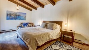A bedroom with a wooden ceiling, a bed with a patterned bedspread, a nightstand with a lamp, and a painting on the wall. - Singing Pines in Marla Bay - Walk to Lake! (Zephyr Cove)
