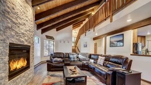 A cozy living room with a stone fireplace, leather sectional sofa, and a staircase leading to an upper level. - Singing Pines in Marla Bay - Walk to Lake! (Zephyr Cove)