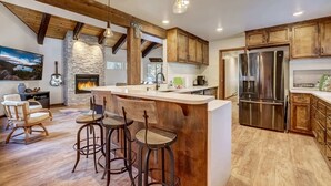 A modern kitchen with a stone fireplace, wooden beams, and a large island with bar stools. - Singing Pines in Marla Bay - Walk to Lake! (Zephyr Cove)