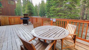 A wooden deck with a round table and chairs, a grill, and a wooden fence. - Whispering Pines Cabin - Family and pet Friendly Abode (South Lake Tahoe)
