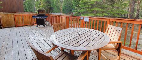 A wooden deck with a round table and chairs, a grill, and a wooden fence.