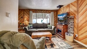 A cozy living room with a fireplace, a sofa, a coffee table, and a television. - Whispering Pines Cabin - Family and pet Friendly Abode (South Lake Tahoe)