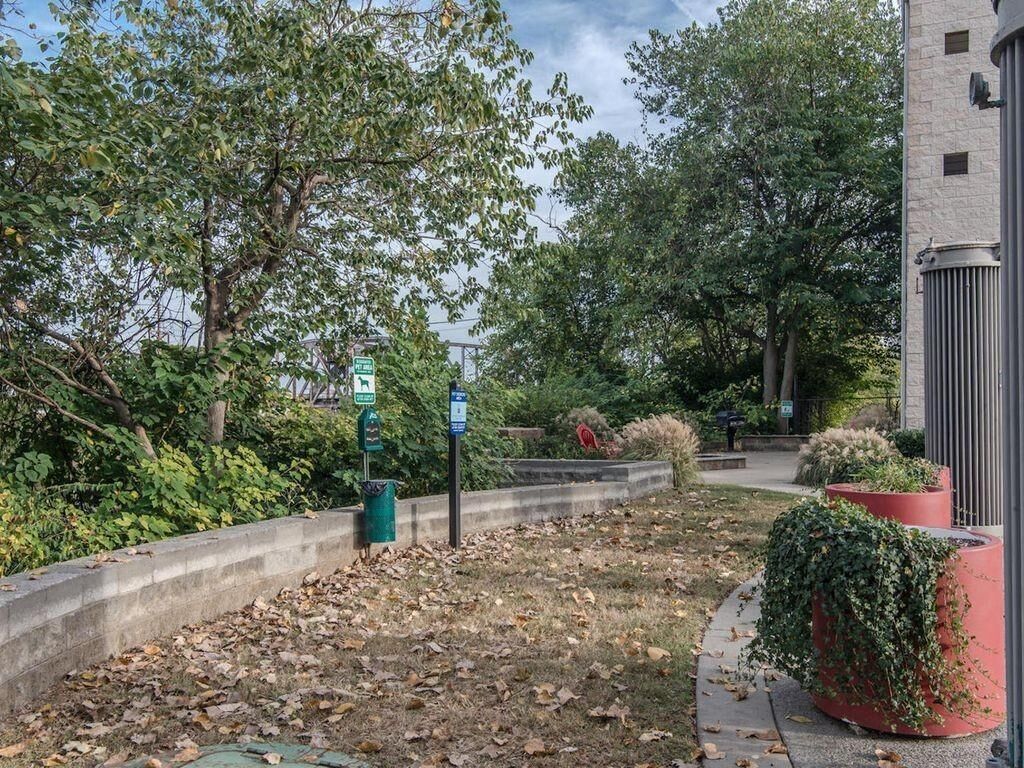 A landscaped area with a concrete pathway, leaf-covered ground, and a building with a cylindrical structure on the right.