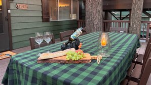 Una mesa al aire libre con mantel a cuadros, una botella de vino, copas, una botella de agua, botellas de champán y vino alternándose.