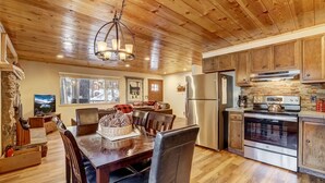 Una cocina con paneles de madera, comedor, chimenea de piedra y ventanas amplias.
