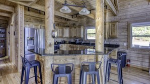 Una cocina amplia con paredes de madera, una isla central con taburetes de bar, electrodomésticos de acero inoxidable y ventanas grandes.