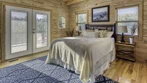 Un dormitorio con paneles de madera, una cama grande, dos mesitas de noche con lámparas y una ventana con vistas a árboles.