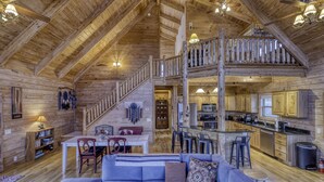 Interior de una cabaña de troncos con comedor, cocina y dormitorio en loft.