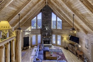 A cozy loft-style room with a stone fireplace, wooden beams, large windows, a sofa, a TV, and a dining area. - The Aviary a Stargazers Dream✨ Close to Downtown 🛍️ Orchards 🍎 Train 🚂 Golf ⛳ (Morganton)