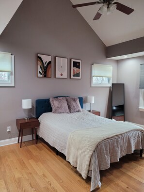 A bedroom with a bed, two nightstands, a ceiling fan, and three wall-mounted artworks.