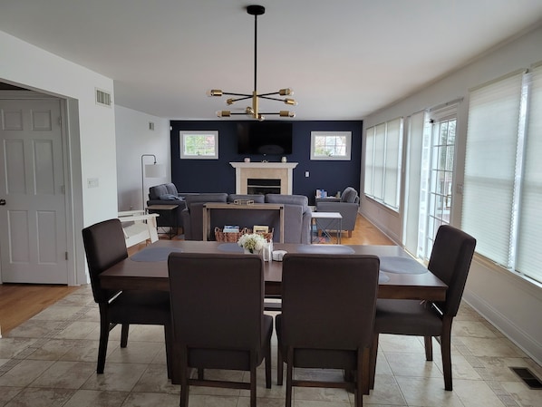 A dining area with a rectangular table and four chairs, a sofa, and a fireplace in the background.