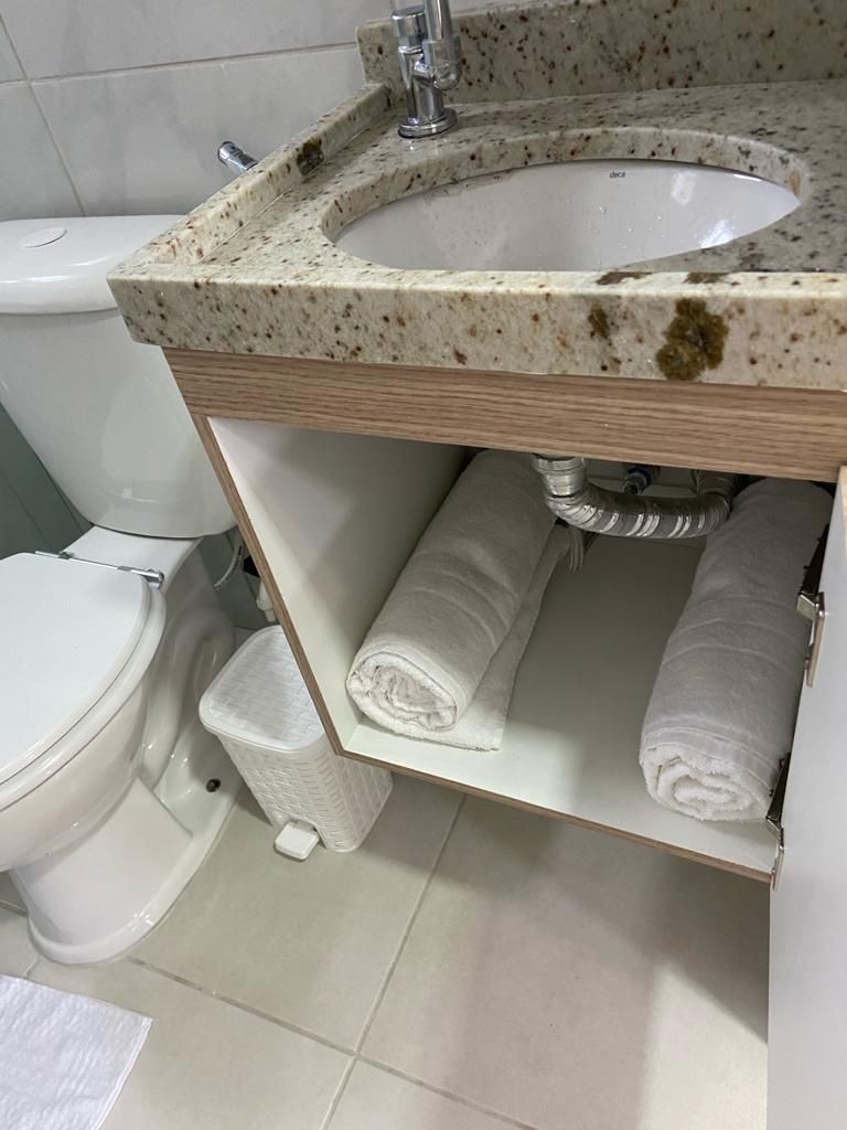 Een badkamer met een wit wastafel, toilet en een plank met opgerolde handdoeken.