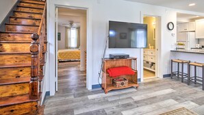 A spacious living area with a wooden staircase, a large flat-screen TV, a kitchen with white cabinets, and a dining area with bar stools. - Peaceful Hurley Retreat ~ 1 Mi to Main Street (Hurley)