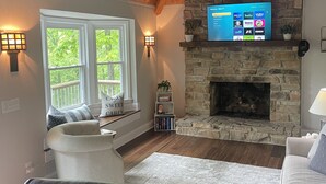 A cozy living room with a stone fireplace, a mounted TV, and comfortable seating. - The Cozy Cottage on Little Duck Cove (Roxboro)