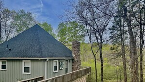 A house with a stone chimney, a wooden deck, and a stone pathway leading to the entrance. - The Cozy Cottage on Little Duck Cove (Roxboro)