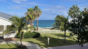 A residential property with a view of the ocean, palm trees, and a white fence.