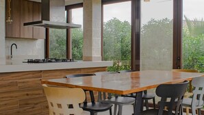 A modern kitchen with a large island, wooden cabinets, and a view of greenery outside.