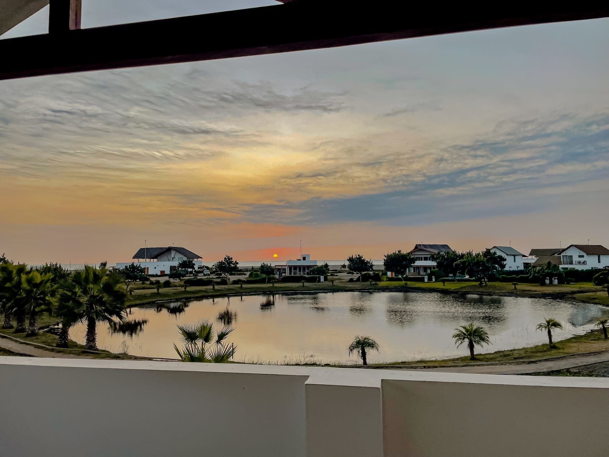Vista de un lago con casas al fondo y un atardecer.