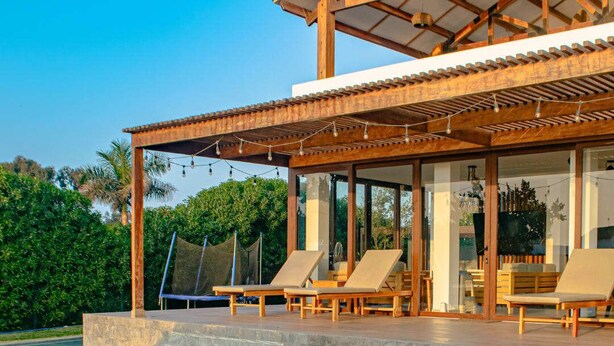 A modern outdoor pool area with a wooden pergola, lounge chairs, and a clear view of the surrounding greenery.