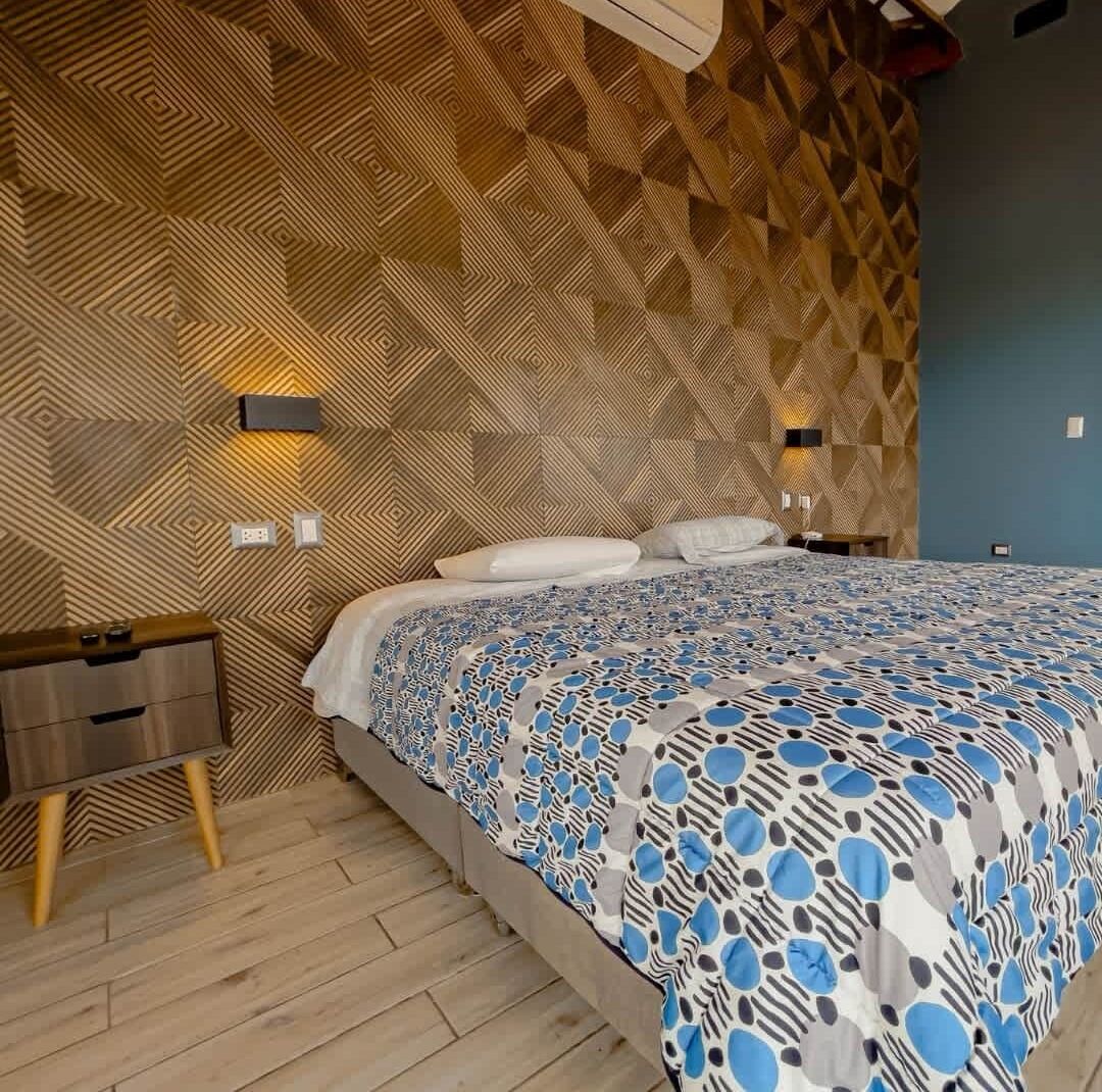Ein modernes Schlafzimmer mit einer Wand im geometrischen Muster, einem großen Bett mit einer blau-weißen Bettdecke und einem Nachttisch aus Holz.