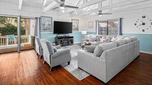 Ein geräumiges Wohnzimmer mit grauem Sofa, Sesseln und einem Flachbildfernseher.
