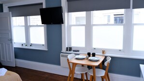 Un comedor con una mesa y sillas, un televisor montado en la pared y ventanas con persianas.