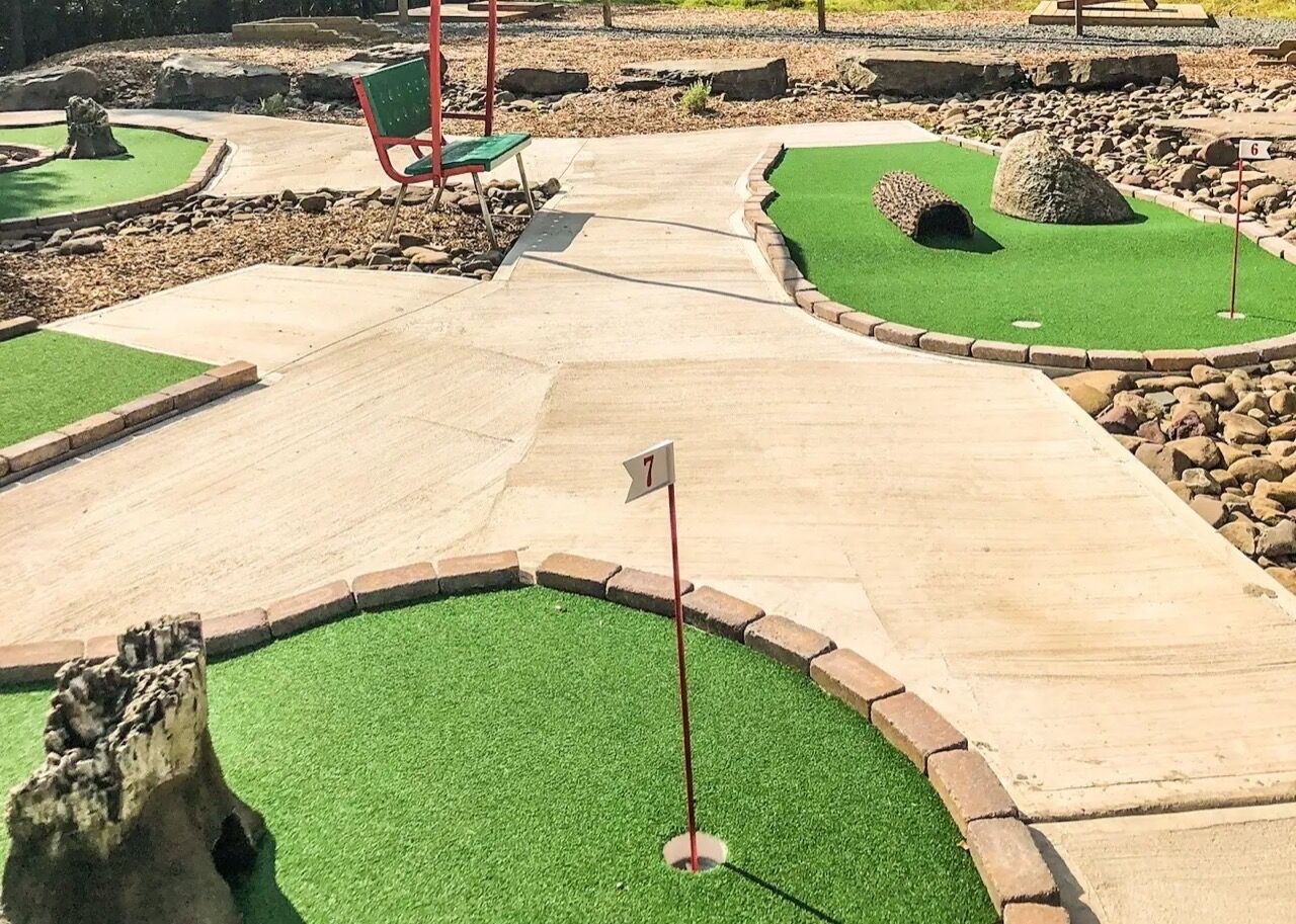 A miniature golf course with numbered holes, green artificial turf, and surrounding landscaping.
