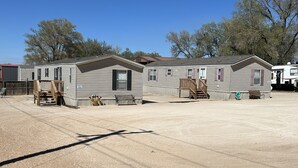 A row of mobile homes with a dirt ground, wooden decks, and a clear blue sky. - Just Dune It - East Home (Waynoka)