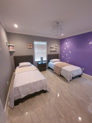 Two single beds with matching headboards and footboards, each dressed in white linens, are situated in this serene bedroom.