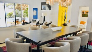 A modern dining area with a large rectangular table surrounded by eight chairs, a large window with a view of a pool and greenery, and a yellow accent wall. - Exclusive Beach Front Luxe Boutique Retreat (Bahia de Banderas)