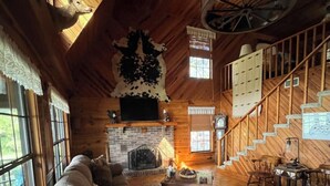 A cozy log cabin interior with a fireplace, wooden furniture, and a spiral staircase.