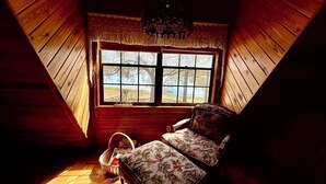 A cozy attic bedroom with a wooden sloped ceiling, a large window with a view of trees, and a floral-patterned bed.