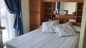 Un dormitori amb un llit, roba de llit a ratlles, un armari de fusta i una finestra amb cortines.